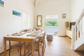 A dining area with a wooden table and chairs, a small round table, and a view of the outdoors through a door. - Charming duplex with a view of the marina and the cistern (Le Gosier)