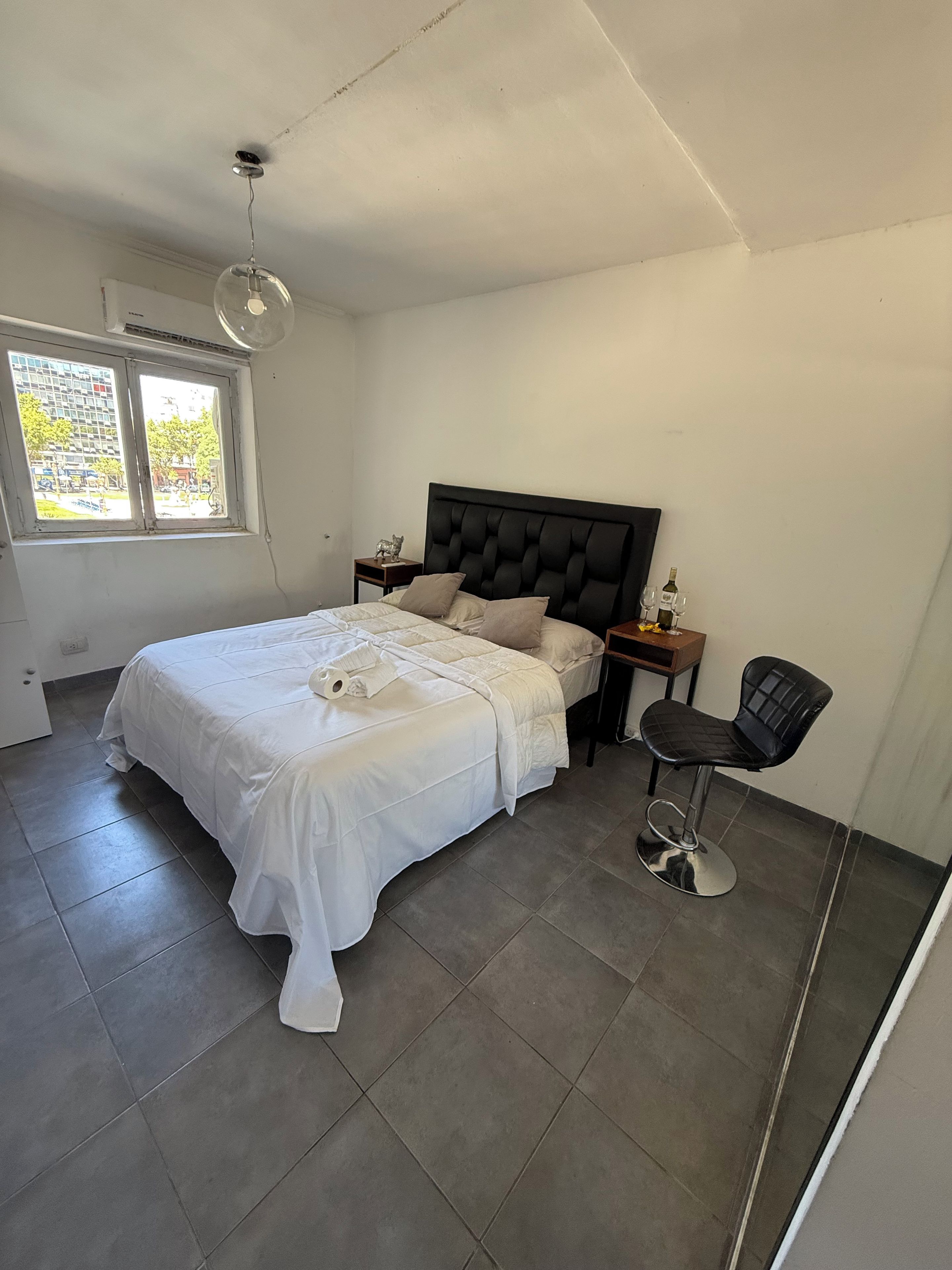 A bedroom with a bed, a nightstand, a chair, and a window.