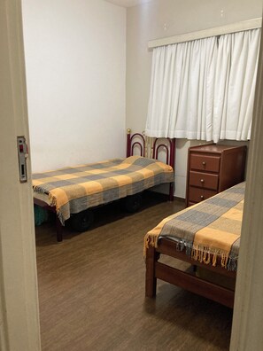 A room with two single beds, a wooden dresser, a white curtain, and a door with a lock. - Apartment in Guarujá - Enseada Beach - Excellent (Guarujá)