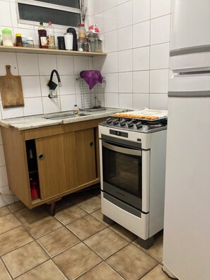 A kitchen with a stove, oven, and a sink. There are cabinets, a countertop, and a window above the sink. - Apartment in Guarujá - Enseada Beach - Excellent (Guarujá)