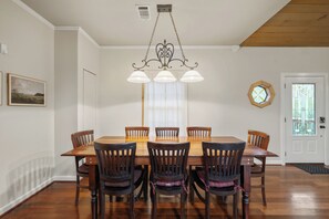 A dining room with a wooden table and chairs, a chandelier, a clock, and a door with a stained glass window. - Private Lakefront Retreat | Pool, Hot Tub, Kayaks (Hot Springs)