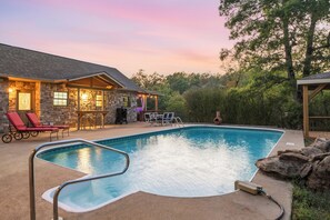 A swimming pool with a stone house in the background, outdoor seating, and a covered area. - Private Lakefront Retreat | Pool, Hot Tub, Kayaks (Hot Springs)