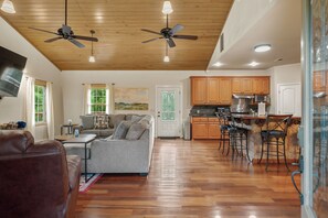 A spacious living area with a sofa, a dining table, and a kitchen with wooden cabinets and a bar area. - Private Lakefront Retreat | Pool, Hot Tub, Kayaks (Hot Springs)