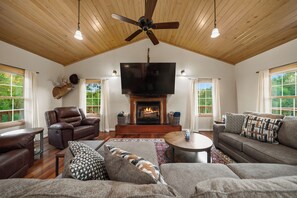 A spacious living room with a fireplace, leather sofa, and a mounted television. - Private Lakefront Retreat | Pool, Hot Tub, Kayaks (Hot Springs)