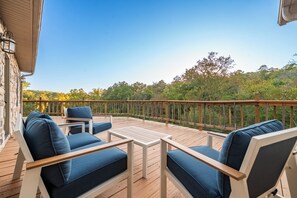 Eine Holzterrasse mit Gartenmöbeln, einem Geländer und Blick auf Bäume und Hügel.