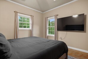 A bedroom with a bed, two windows with curtains, a flat-screen TV mounted on the wall, and a visible power outlet. - Private Lakefront Retreat | Pool, Hot Tub, Kayaks (Hot Springs)