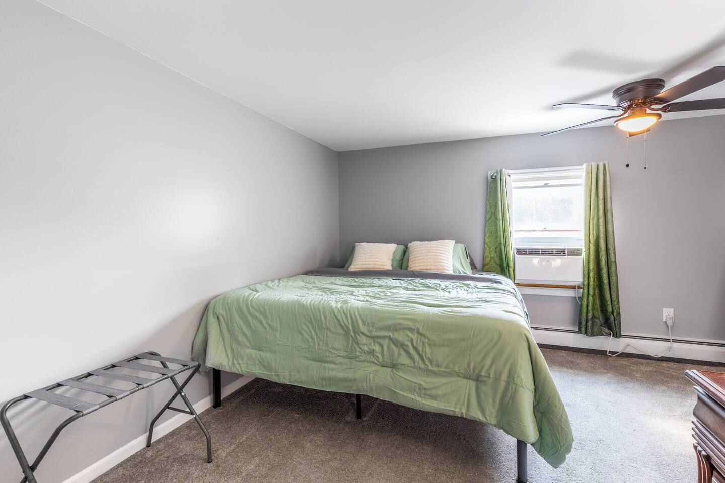 A bedroom with a bed, a ceiling fan, a window with curtains, and a radiator.