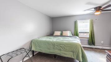 A bedroom with a bed, a ceiling fan, a window with curtains, and a radiator.