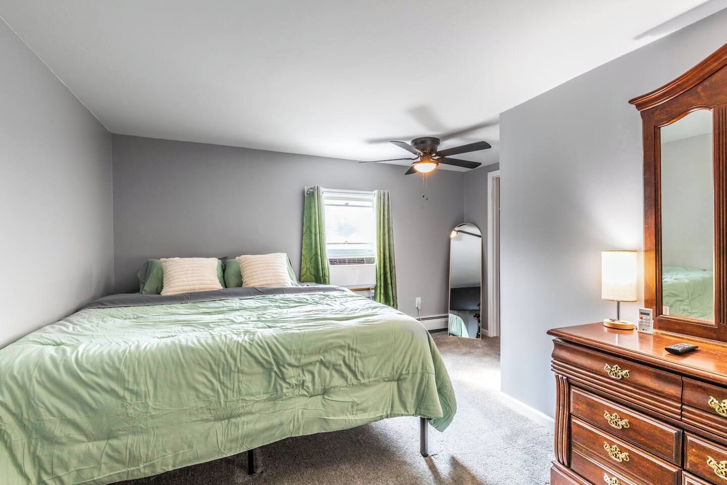 Une chambre à coucher comprenant un lit, une commode, un ventilateur de plafond et une fenêtre avec des rideaux.