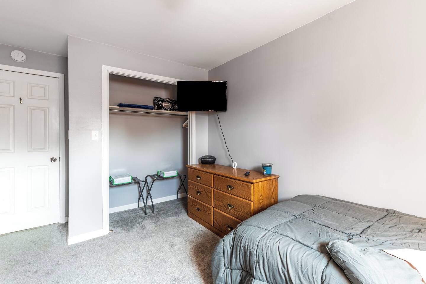 Une chambre à coucher comprenant un lit, une commode, un bureau avec des chaises et un téléviseur fixé au mur.