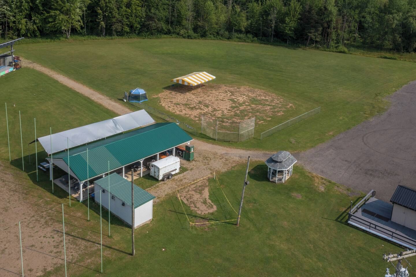 Un terrain de sport doté d’une zone de sièges abritée, d’un petit pavillon et d’une zone délimitée par une clôture.