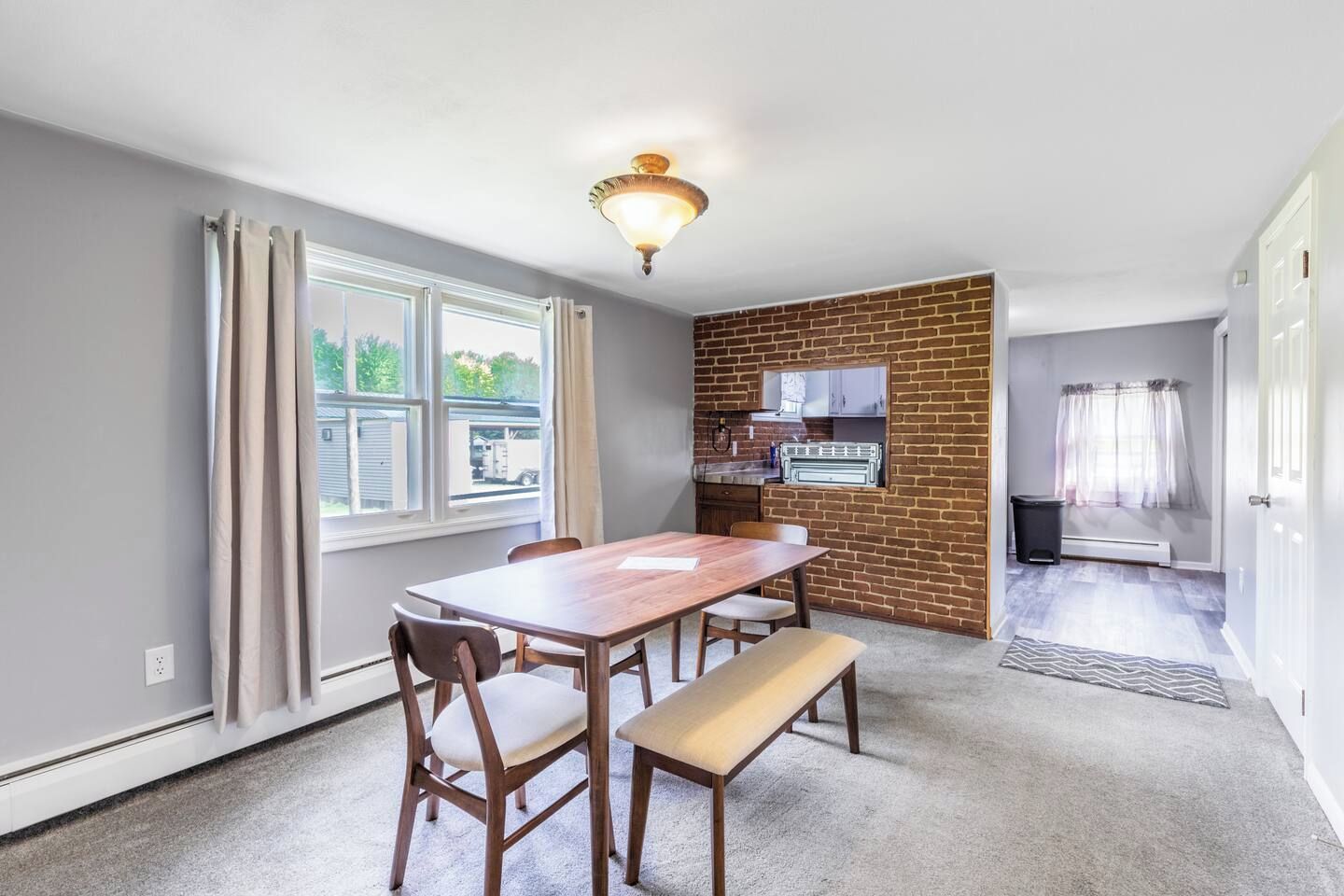 Une cuisine de taille réduite avec un mur d’accent en briques, un coin repas avec une table et des chaises en bois, et une vue sur l’extérieur par une fenêtre.