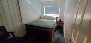 A small, narrow room with a bed, a chair, a window with blinds, and a radiator. - North Pole Getaway + 2 bd Home w/ Double Garage (Fairbanks)