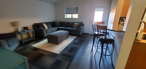 A living room with a sofa, ottoman, and a dining area with chairs. - North Pole Getaway + 2 bd Home w/ Double Garage (Fairbanks)