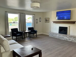 Una sala de estar con chimenea, televisor de pantalla plana, sofá, mesa de comedor con sillas y vistas al exterior a través de una ventana.