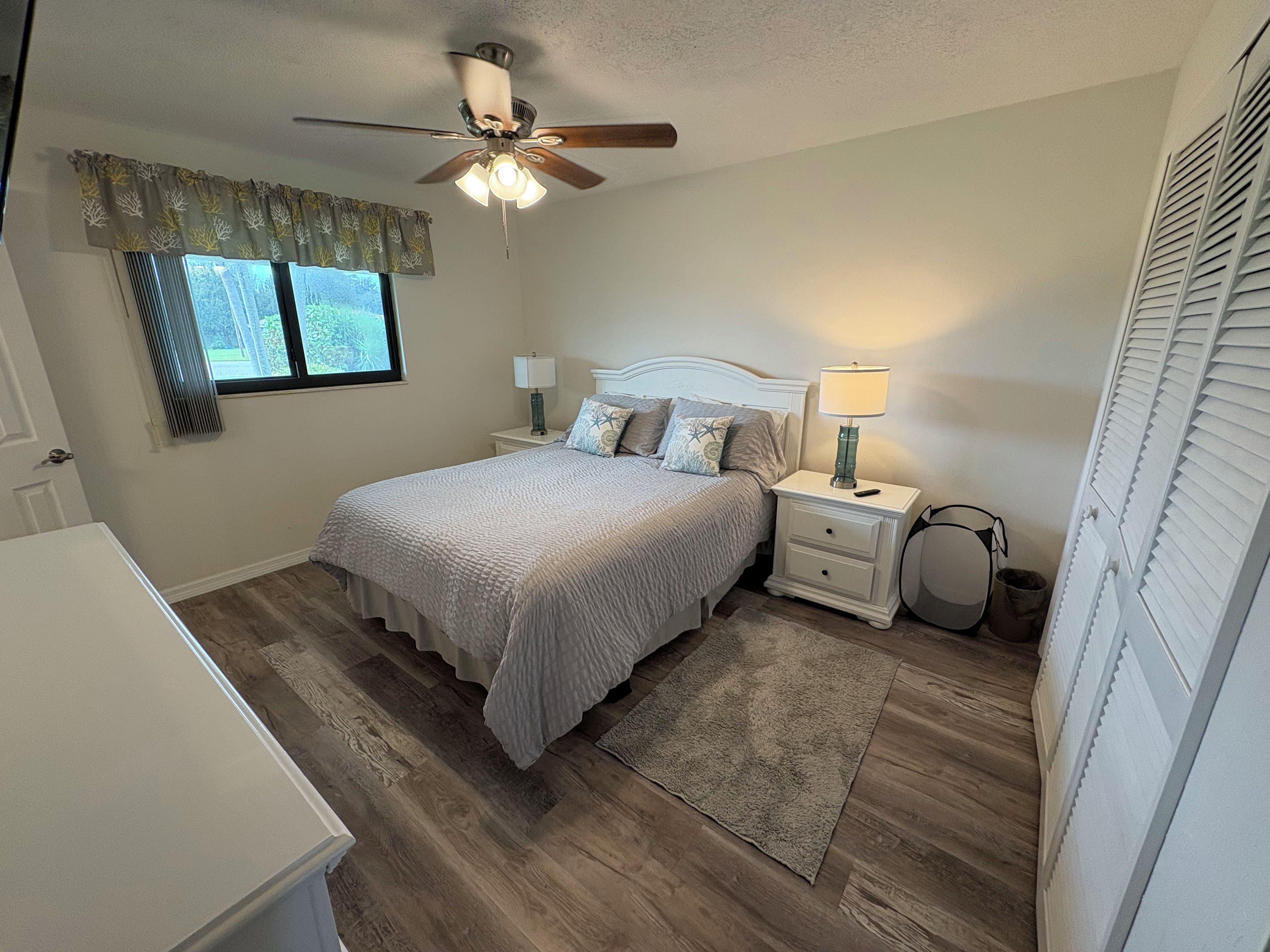 A bedroom with a bed, nightstands, a ceiling fan, a window with curtains, and a radiator.