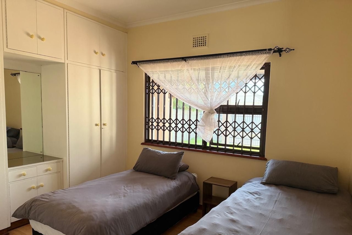 Een slaapkamer met twee eenpersoonsbedden, een garderobe en een raam met decoratieve roede.