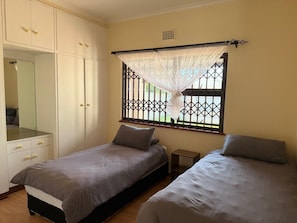 Een slaapkamer met twee eenpersoonsbedden, een garderobe en een raam met decoratieve roede.