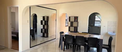 Un comedor moderno con una mesa grande y sillas, una cocina con ventana y un espejo que refleja la habitación.