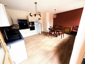 A modern kitchen with a dining area, wooden flooring, and a red accent wall. - Downtown ground-floor apartment (La Chapelle-en-Vercors)