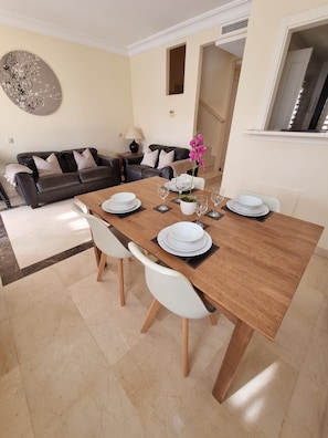 A dining area with a wooden table set for four, white chairs, and a modern decor including a wall art piece and a potted plant. - Sunny Spanish Escape – 2-Bed Townhouse with Stunning Pool Views (San Javier)
