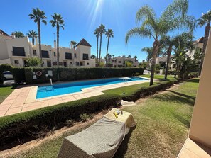 A swimming pool with a clear blue water, surrounded by a well-maintained lawn and palm trees. - Sunny Spanish Escape – 2-Bed Townhouse with Stunning Pool Views (San Javier)