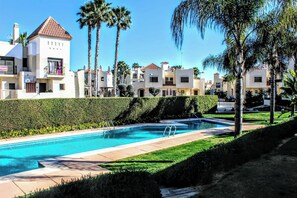 Une piscine à l’eau d’un bleu cristallin, entourée d’une haie bien entretenue et de palmiers.