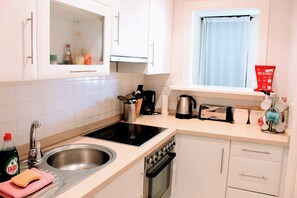 Une cuisine avec des meubles blancs, un évier en acier inoxydable, une cuisinière et une fenêtre avec un rideau.