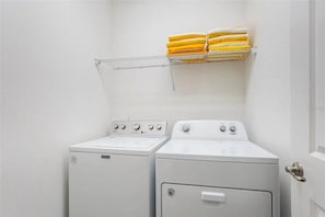 Une buanderie avec deux machines à laver blanches et un étendoir métallique sur lequel sont pliées des serviettes.