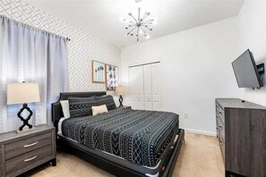 Une chambre à coucher comprenant un lit, une table de chevet, une commode et un téléviseur fixé au mur.