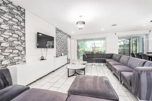 Una sala de estar moderna con una pared de acento de piedra, un televisor de pantalla plana, un sofá modular y un vidrio que da al exterior.