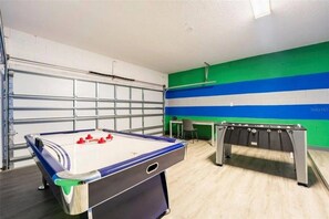 A room with a foosball table, a desk, and a garage door. - 10 BD/ 8 BA/ Sonoma Resort - 2613 CA (Kissimmee)