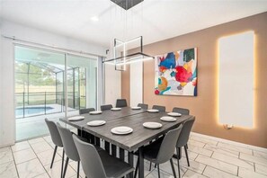 A modern dining room with a large table set for 12, surrounded by chairs, with a glass door leading to an outdoor area. - 10 BD/ 8 BA/ Sonoma Resort - 2613 CA (Kissimmee)