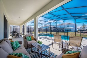 Ein überdachter Patio-Bereich mit Gartenmöbeln, einem Pool und Blick auf umliegende Häuser.