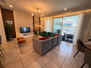 A modern living room with a flat-screen TV, a sofa, a dining area, and a view of the outdoors. - Corner-Lot 5 BD/ 4.5 BA/ Windsor Island - 1000 PD (Davenport)