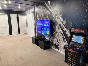A room with a large screen displaying a TV interface, a gaming console, and a wall mural. - Corner-Lot 5 BD/ 4.5 BA/ Windsor Island - 1000 PD (Davenport)