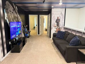 A room with a large flat-screen TV on a stand, a black sofa with blue cushions, and a wall mural. - Corner-Lot 5 BD/ 4.5 BA/ Windsor Island - 1000 PD (Davenport)