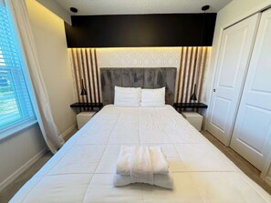A hotel room with a large bed, a headboard with vertical slats, bedside tables, and a window with blinds. - Corner-Lot 5 BD/ 4.5 BA/ Windsor Island - 1000 PD (Davenport)