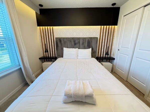 A hotel room with a large bed, a headboard with vertical slats, bedside tables, and a window with blinds. - Corner-Lot 5 BD/ 4.5 BA/ Windsor Island - 1000 PD (Davenport)