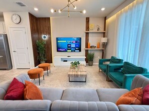 A modern living room with a flat-screen TV, sofas, a coffee table, and a plant. - Corner-Lot 5 BD/ 4.5 BA/ Windsor Island - 1000 PD (Davenport)