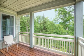 A wooden deck with a white railing, a bench, and a window overlooking a forested area. - 2BR/2BA Suite at Smugglers' Notch · Three Mountains · Heated Pool (Jeffersonville)