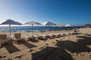A beach with sun loungers and umbrellas, a clear sky, and the ocean in the background. - Jr Suite at The Club at Hacienda del Mar (Cabo San Lucas)