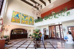 A lobby with a reception desk, a chandelier, artwork on the walls, and a potted plant. - Jr Suite at The Club at Hacienda del Mar (Cabo San Lucas)