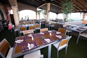 An outdoor dining area with tables set for guests, featuring a mix of chairs and benches, and a covered section with a view. - Jr Suite at The Club at Hacienda del Mar (Cabo San Lucas)
