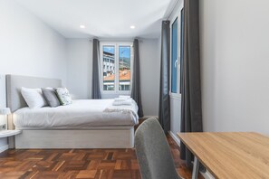 A hotel room with a bed, a bedside table, a chair, and a view of buildings through a window. - Chez Agostinha by Atlantic Holiday (Funchal)