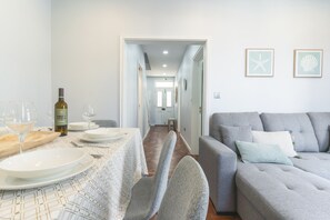 Ein Essbereich mit einem Tisch für zwei Personen, einer Weinflasche und einer Couch im Hintergrund.