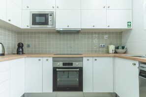 A modern kitchen with white cabinets, a built-in microwave, a coffee maker, and an oven. - Chez Agostinha by Atlantic Holiday (Funchal)