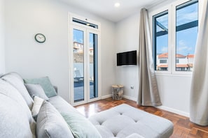 A modern living room with a sofa, a small round table, a TV mounted on the wall, and a window with curtains. - Chez Agostinha by Atlantic Holiday (Funchal)