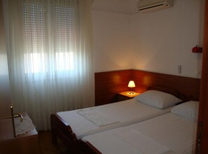 A hotel room with two beds, a nightstand with a lamp, a window with sheer curtains, and an air conditioning unit on the wall. - Superior One Bedroom Apartment with Balcony and Sea View (Petrcane)