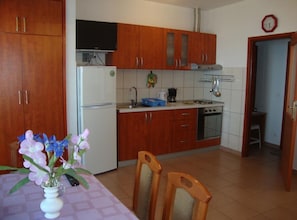 Una cocina con armarios de madera, un refrigerador, una estufa y una zona de comedor con sillas y una mesa.